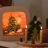 A Toverlux Magic Lamp with a Christmas tree Silhouette with artwork By Gwen van Knippenberg inside. The lamp is on and had a decorated Grimm's celebration ring placed in front of it.
