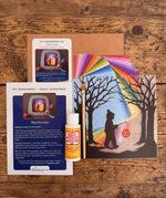 Toverlux Martinmas Silhouette DIY craft kit content laid out on a wooden surface. The kit includes silhouette panel with child carrying a lantern through a forest design, 20 sheets of coloured paper, paint brush, mod podge glue sealer and a step by step instruction guide booklet.