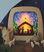 A Toverlux DIY Transparencies with  Winter nativity artwork shown in a wooden magic lamp. Ostheimer wooden toys have been placed in front of it.