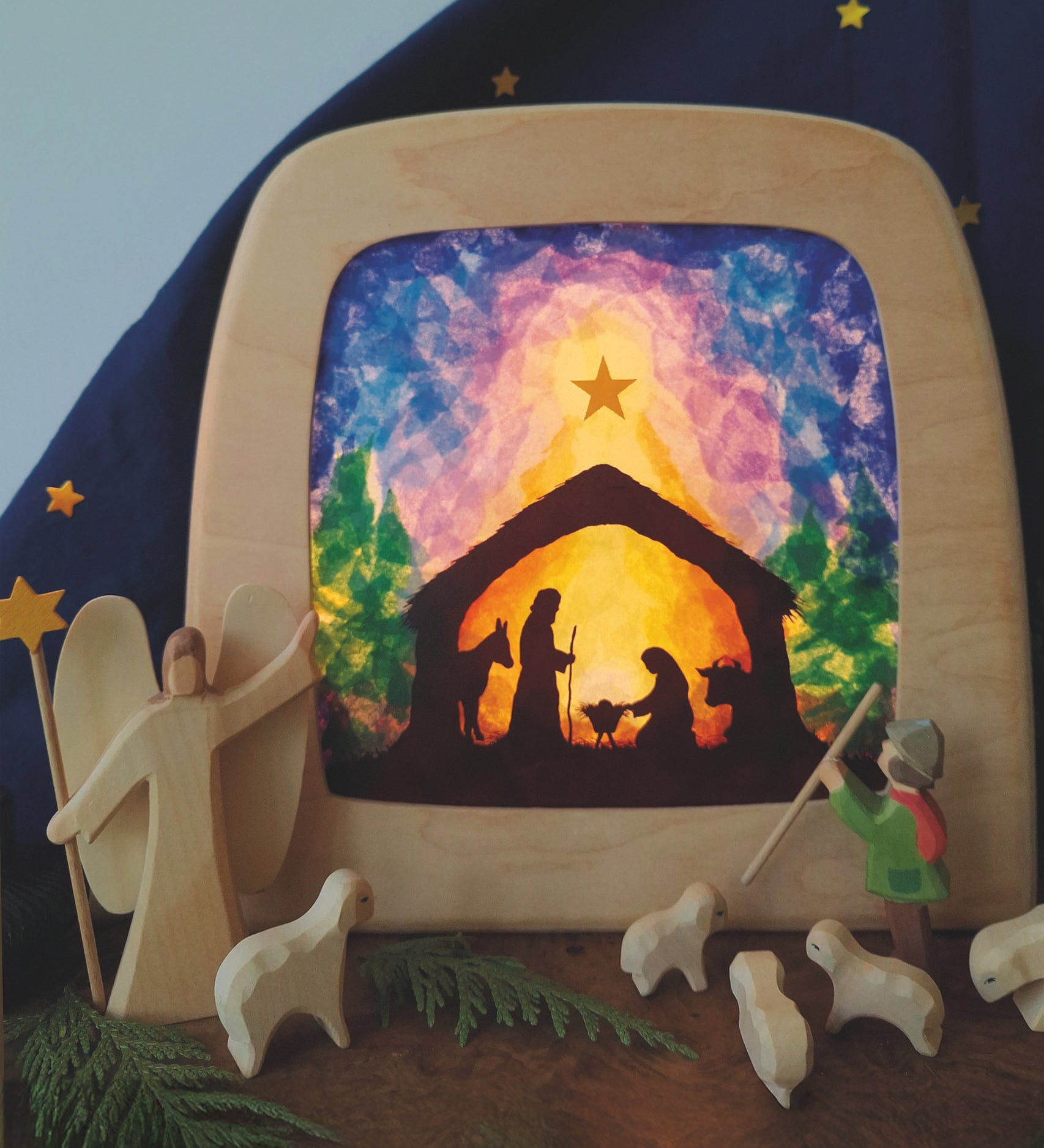 A Toverlux DIY Transparencies with  Winter nativity artwork shown in a wooden magic lamp. Ostheimer wooden toys have been placed in front of it.