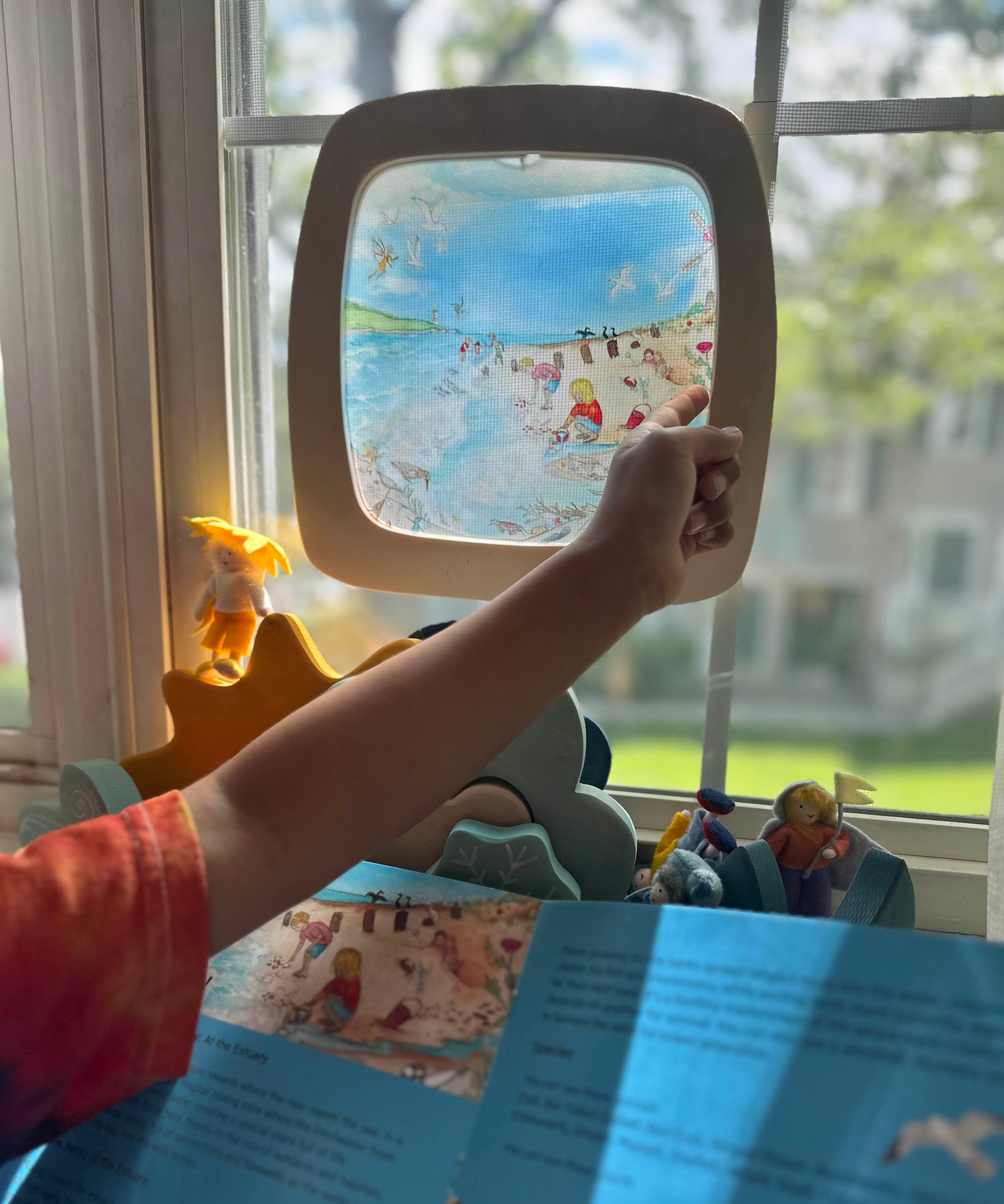 Toverlux Edulux watercycles silhouette featuring Stephanie Green's Estuary artwork shown in a wooden magic window frame. A Grimm's weather set has been set up on the windowsill underneath. A child's hand can be seen pointing at some of the details in the artwork.
This silhouette is part of a wide range of Toverlux silhouettes available here at Babipur. 