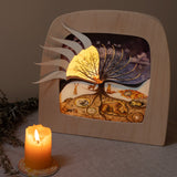 A cosy and warm display with the Toverlux 12 holy nights silhouette inside a lamp. Silhouettes has the windows open revealing a festive illustration inside. Both are available at Babipur.