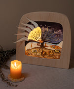 A cosy and warm display with the Toverlux 12 holy nights silhouette inside a lamp. Silhouettes has the windows open revealing a festive illustration inside. Both are available at Babipur.