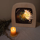 A warm cosy display with the Toverlux advent calendar inside a wooden lantern both available at Babipur. Lantern is standing on a table cloth next to a lit candle. 