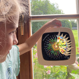 A girl opening a window on the Toverlux advent calendar revealing the silhouette underneath. The silhouette is in a Toverlux wooden magic frame and hanging on a window. Both are available at Babipur.