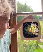 A girl opening a window on the Toverlux advent calendar revealing the silhouette underneath. The silhouette is in a Toverlux wooden magic frame and hanging on a window. Both are available at Babipur.
