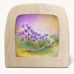 A Toverlux silhouette in the magic lamp, the illustration is of some purple flowers with a dreamy purple and yellow sky in the background.