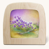 A Toverlux silhouette in the magic lamp, the illustration is of some purple flowers with a dreamy purple and yellow sky in the background.