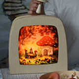 Toverlux magic lamp with a Autumn gnome toadstool picnic silhouette by artist Vogel Geluk. A watercolour style illustration of a toadstool house in a forest with a table with three gnomes sat around it. The silhouette has been placed in a magic lamp on a table. A child can be seen in the background placing Erzi mushrooms on top of the magic lamp.
 A range of Toverlux silhouettes, lamps and accessories are available at Babipur. 
