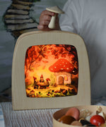 Toverlux magic lamp with a Autumn gnome toadstool picnic silhouette by artist Vogel Geluk. A watercolour style illustration of a toadstool house in a forest with a table with three gnomes sat around it. The silhouette has been placed in a magic lamp on a table. A child can be seen in the background placing Erzi mushrooms on top of the magic lamp.
 A range of Toverlux silhouettes, lamps and accessories are available at Babipur. 