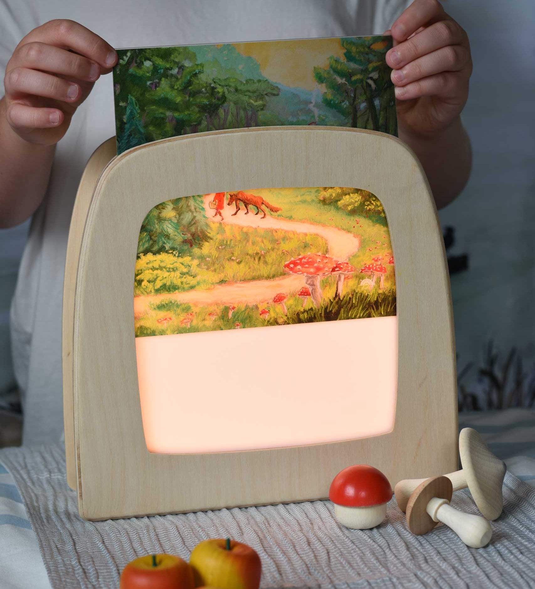 Toverlux Kapitein Kalk - Little Red Riding Hood Silhouette placed in a magic lamp being placed on a table. A beautiful illustration featuring little red hood walking through a forest next to a wolf. 
A range of Toverlux silhouettes, lamps and accessories are available at Babipur.