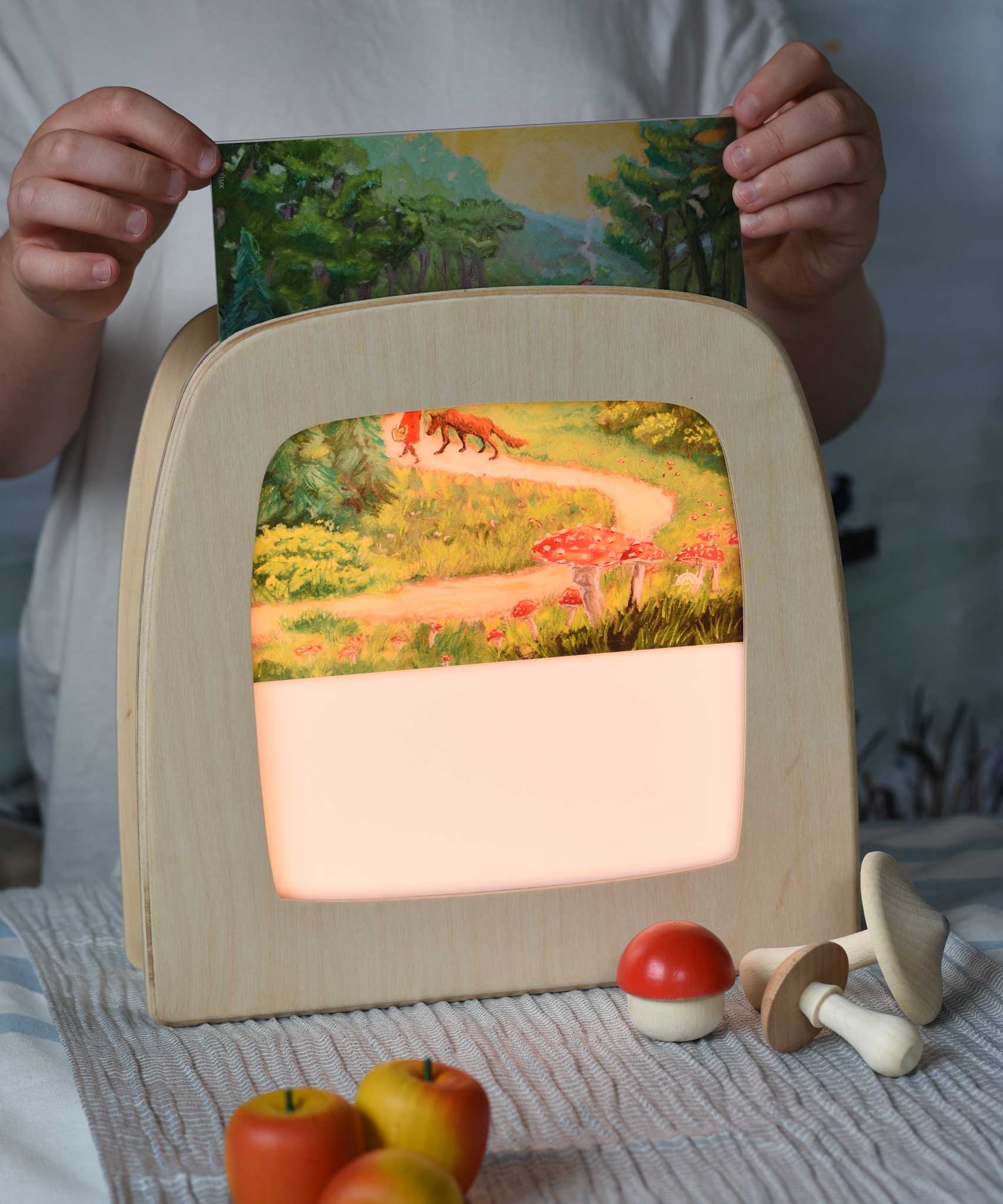 Toverlux Kapitein Kalk - Little Red Riding Hood Silhouette placed in a magic lamp being placed on a table. A beautiful illustration featuring little red hood walking through a forest next to a wolf. 
A range of Toverlux silhouettes, lamps and accessories are available at Babipur.