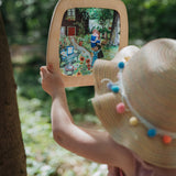 A child standing outside and holding the  Toverlux Artisan Magic Window Frame available at Babipur. Frame has a pastel inspired garden silhouette inside