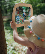 A child standing outside and holding the  Toverlux Artisan Magic Window Frame available at Babipur. Frame has a pastel inspired garden silhouette inside