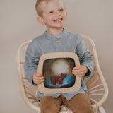 A child sitting on a chair and holding a Toverlux Magic Window Frame  with a brown bear silhouette available at Babipur. 