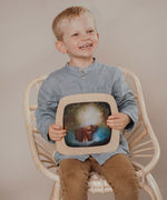 A child sitting on a chair and holding a Toverlux Magic Window Frame  with a brown bear silhouette available at Babipur. 