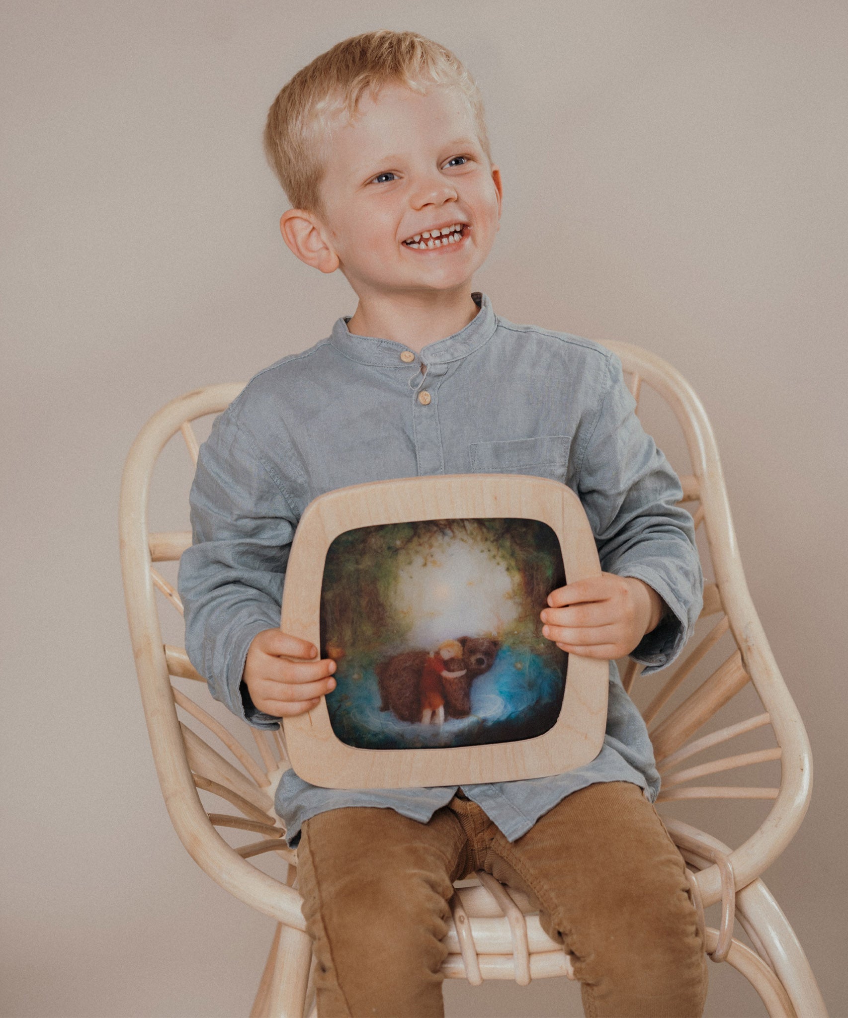 A child sitting on a chair and holding a Toverlux Magic Window Frame  with a brown bear silhouette available at Babipur. 
