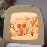 Toverlux silhouette featuring the Christofer's strawberry garden family artwork by Elsa Beskow displayed in a  lit Toverlux lamp. 