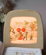 Toverlux silhouette featuring the Christofer's strawberry garden family artwork by Elsa Beskow displayed in a  lit Toverlux lamp. 