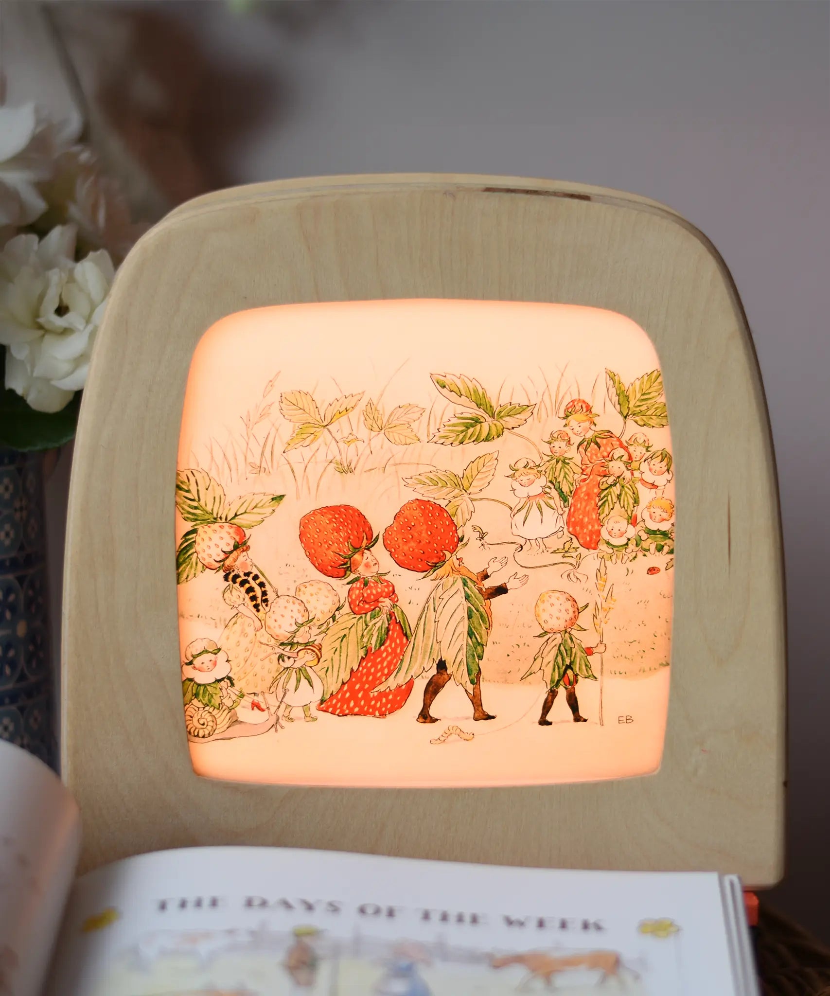 Toverlux silhouette featuring the Christofer's strawberry garden family artwork by Elsa Beskow displayed in a  lit Toverlux lamp. 