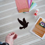Close up of the recycled PET silhouette panel with dove design by Vogel Geluk from the Toverlux Spring dove DIY silhouette transparency craft kit  being held in an adult's hand.