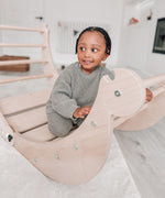 A close up of a Triclimb wooden Archi folding rocker climbing frame with a child sitting inside. Showing the unique joint detail that can be hooked onto a Triclimb pikler climbing frame.