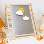 Triclimb-wooden-magnetic Biri board hooked on a Triclimb pikler climbing frame  in a playroom showing various magnetic pieces on the board.