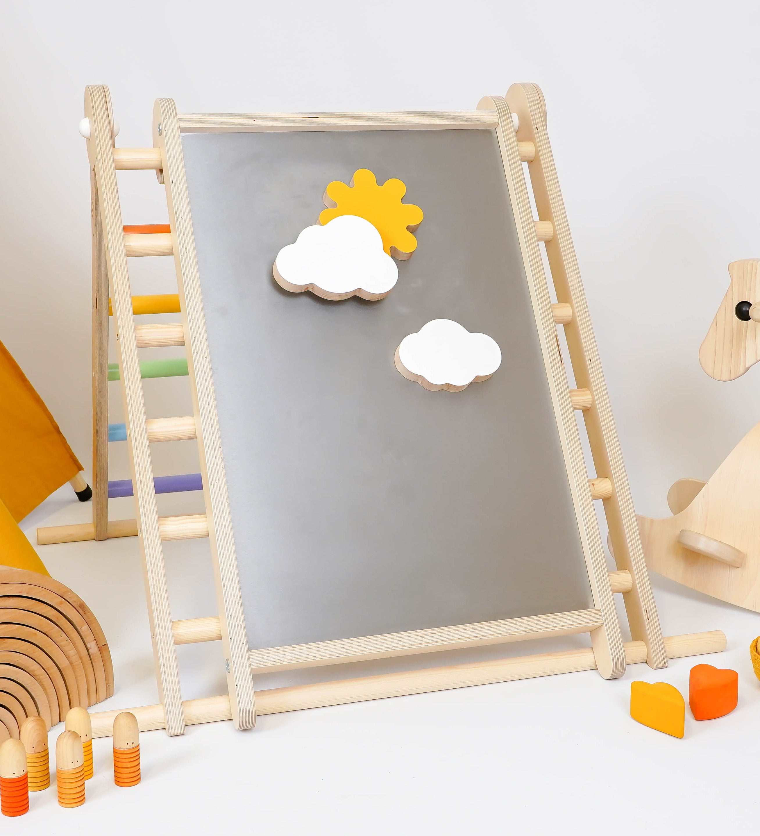 Triclimb-wooden-magnetic Biri board hooked on a Triclimb pikler climbing frame  in a playroom showing various magnetic pieces on the board.