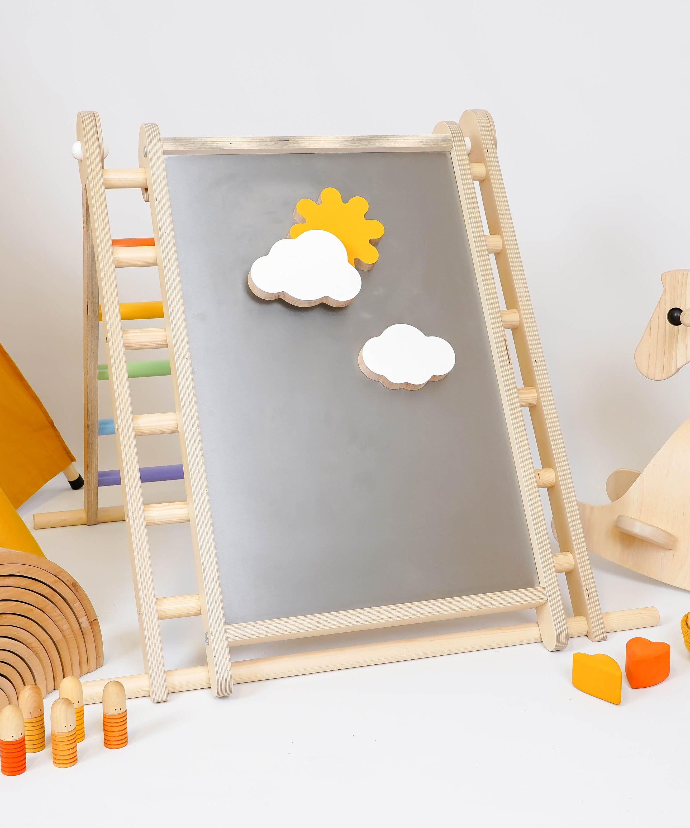 Triclimb-wooden-magnetic Biri board hooked on a Triclimb pikler climbing frame  in a playroom showing various magnetic pieces on the board.