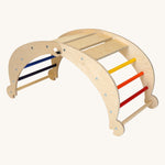 Triclimb wooden folding rocker Archi frame with rainbow coloured rungs including red, orange, yellow, purple blue and green. Features wide wooden slats on top for sitting and attachments on each end to hook onto a Triclimb pikler climbing frame