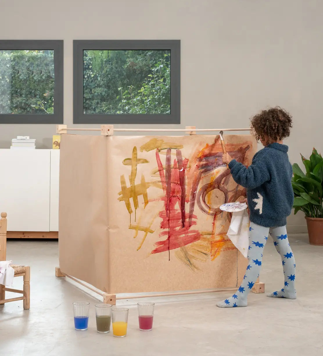 Child painting on paper wrapped around a cube frame made from the Trigonos big frame set standing on a concrete surface