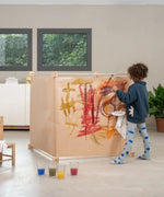 Child painting on paper wrapped around a cube frame made from the Trigonos big frame set standing on a concrete surface