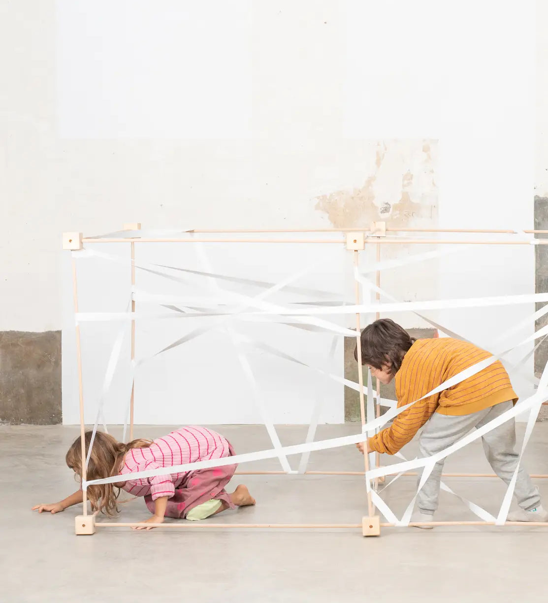 Children playing inside joined cube frames from the Trigonos wooden big frame set on a concrete surface