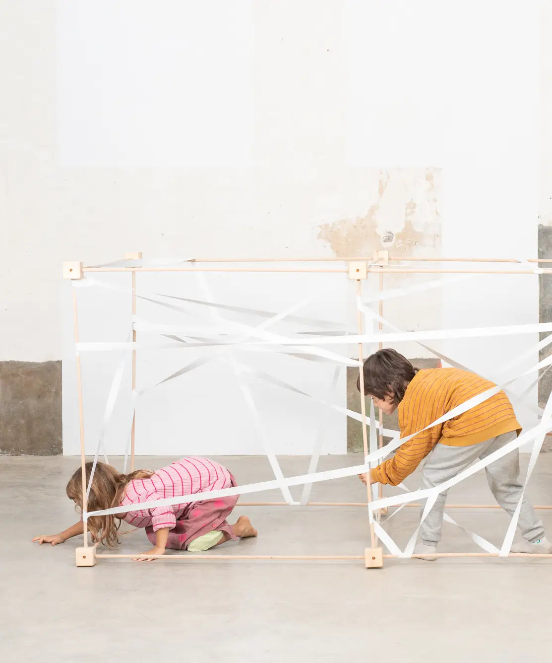 Children playing inside joined cube frames from the Trigonos wooden big frame set on a concrete surface
