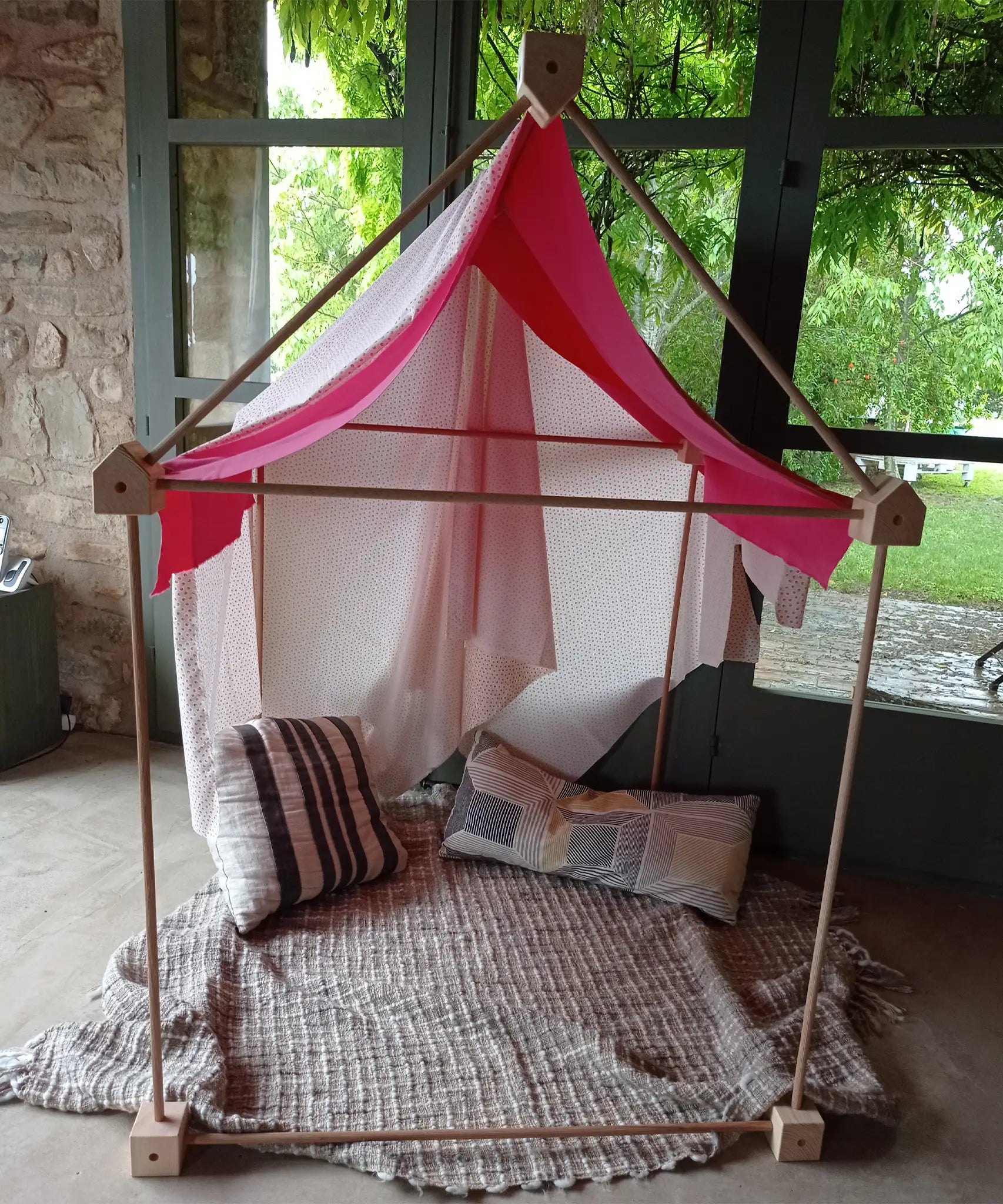 A cosy tent setup made from the Trigonos wooden big start set showing a pink cloth on top of the frame standing on a concrete surface