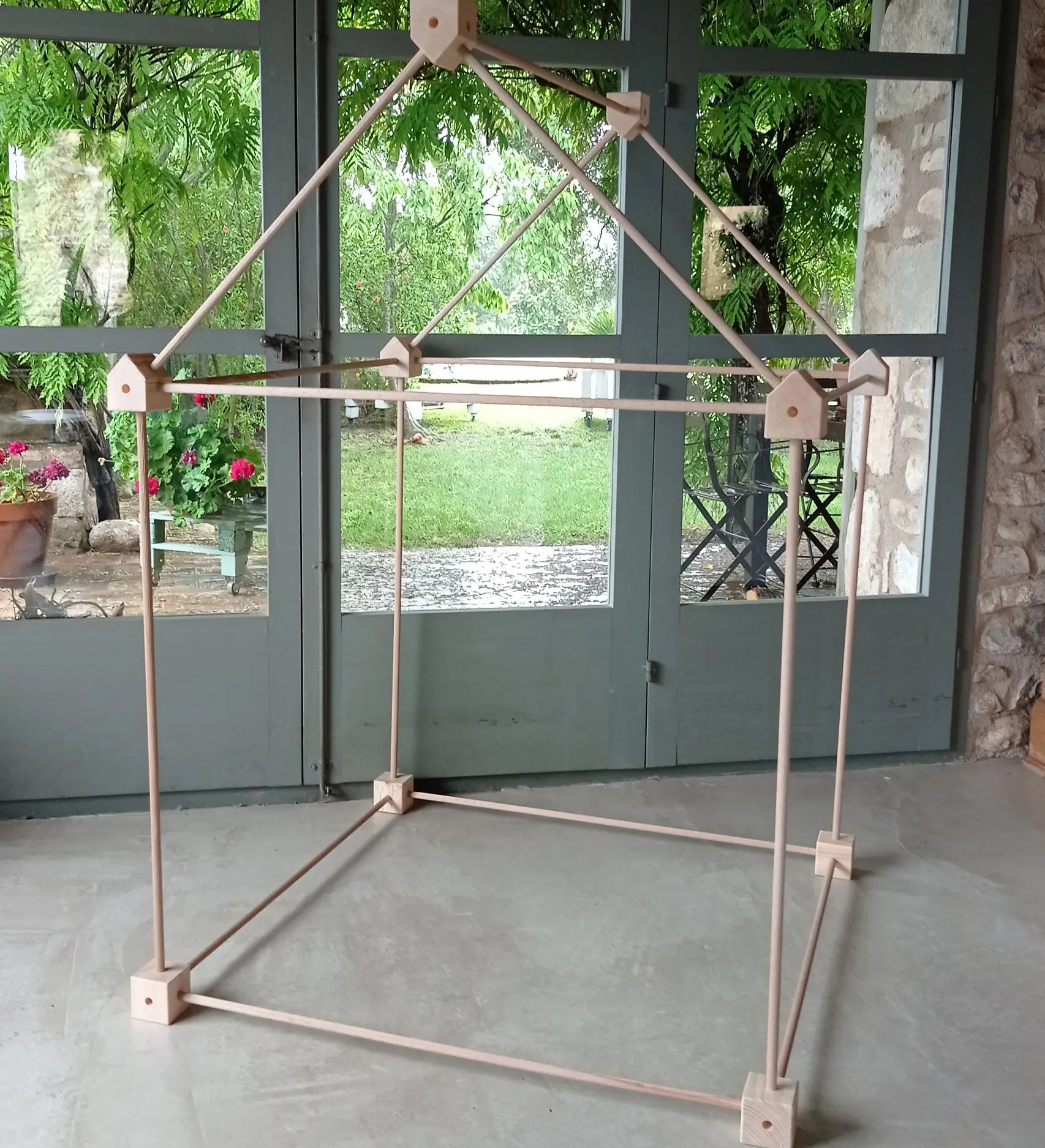 Trigonos big start set showing a tent made up from wooden poles and corner blocks standing on a concrete surface