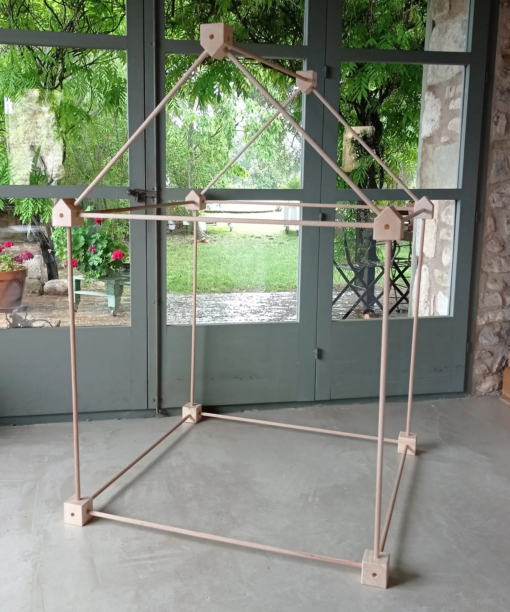 Trigonos big start set showing a tent made up from wooden poles and corner blocks standing on a concrete surface