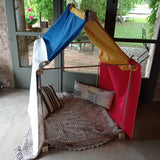 Tent made from the Trigonos wooden big start set showing coloured cloth on top of the frame with cushions and a blanket inside