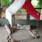 A tent made from the Trigonos wooden big start set showing a white cloth on top of the frame with cushions and a blanket inside