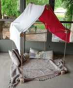 A tent made from the Trigonos wooden big start set showing a white cloth on top of the frame with cushions and a blanket inside