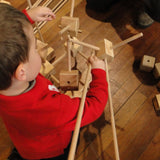 Child building with wooden poles and blocks from the Trigonos starter construction set on a wooden floor