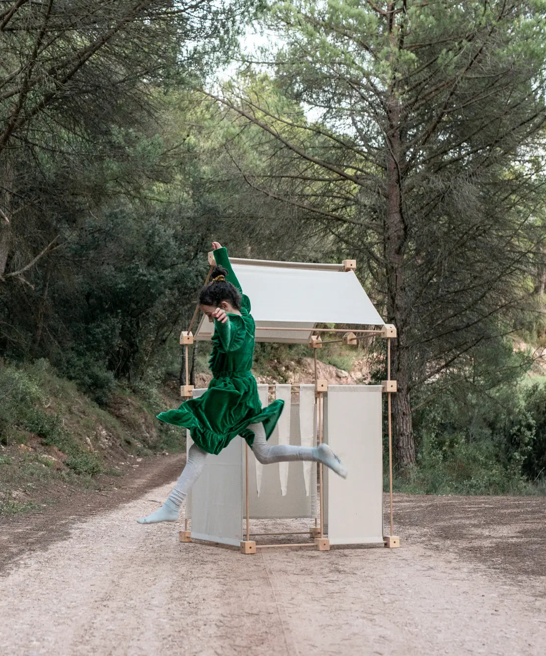 Child jumping in front of a den made from the Trigonos family wooden construction set in a forestry