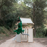 Child jumping in front of a den made from the Trigonos family wooden construction set in a forestry