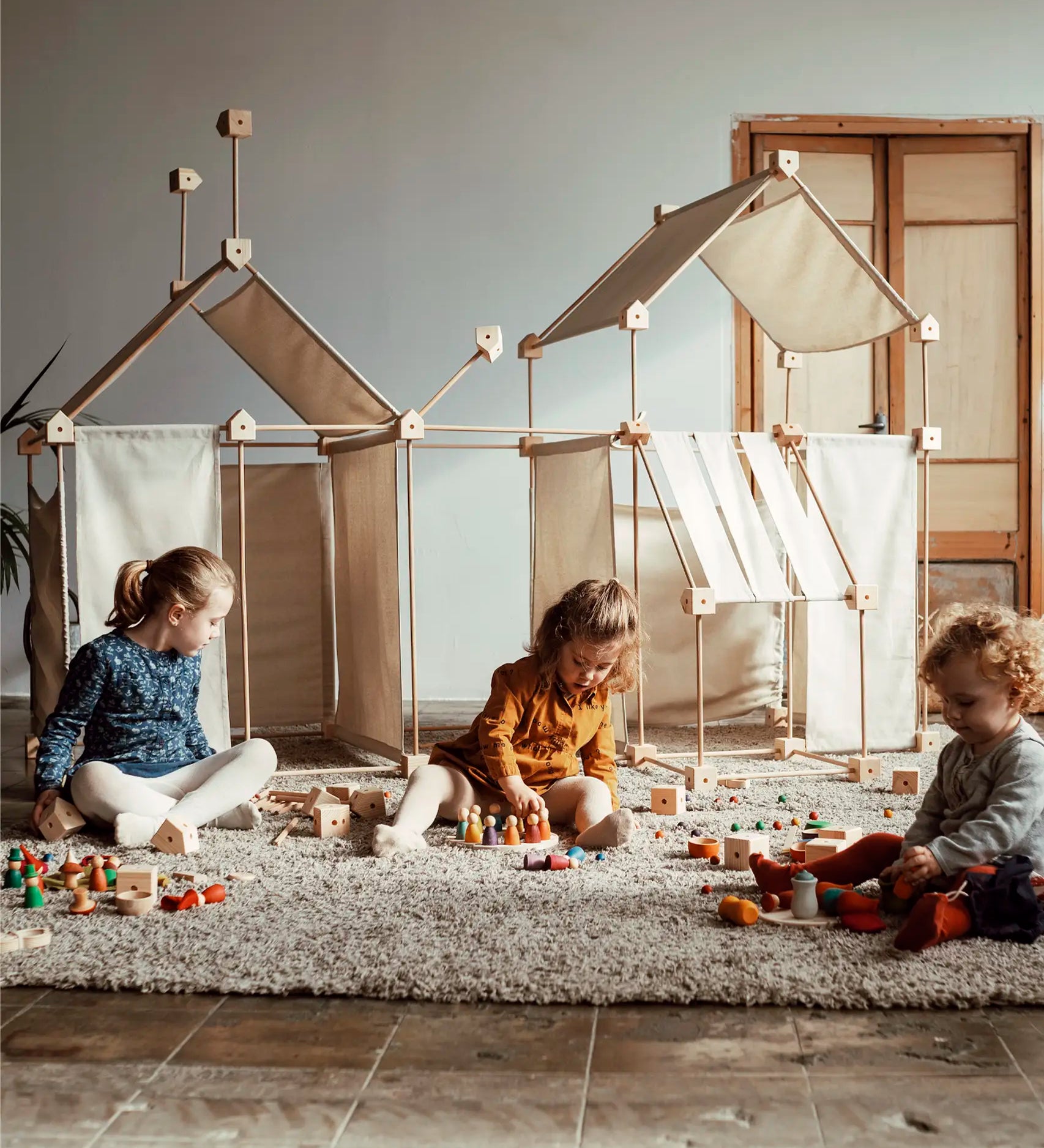 Multiple dens built from the Trigonos family wooden construction set with children playing with wooden toys 