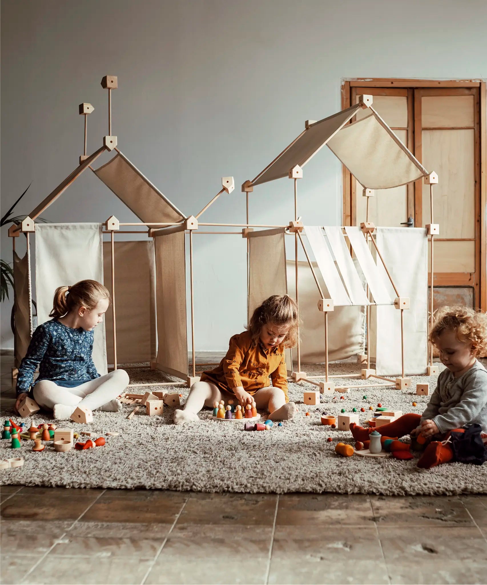 Multiple dens built from the Trigonos family wooden construction set with children playing with wooden toys 