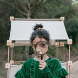 Child standing in front of a den built from the Trigonos family wooden construction set in a forestry