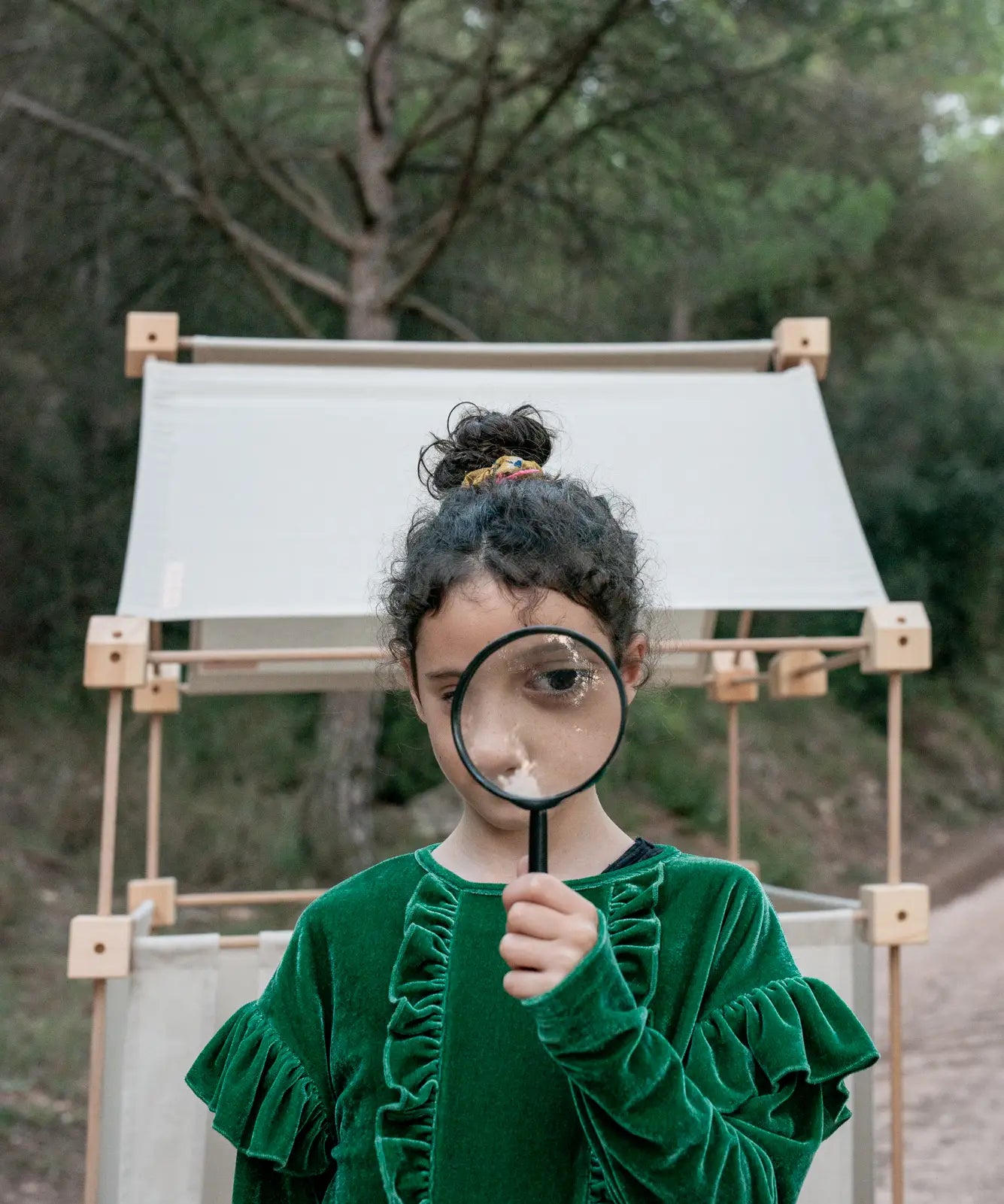Child standing in front of a den built from the Trigonos family wooden construction set in a forestry