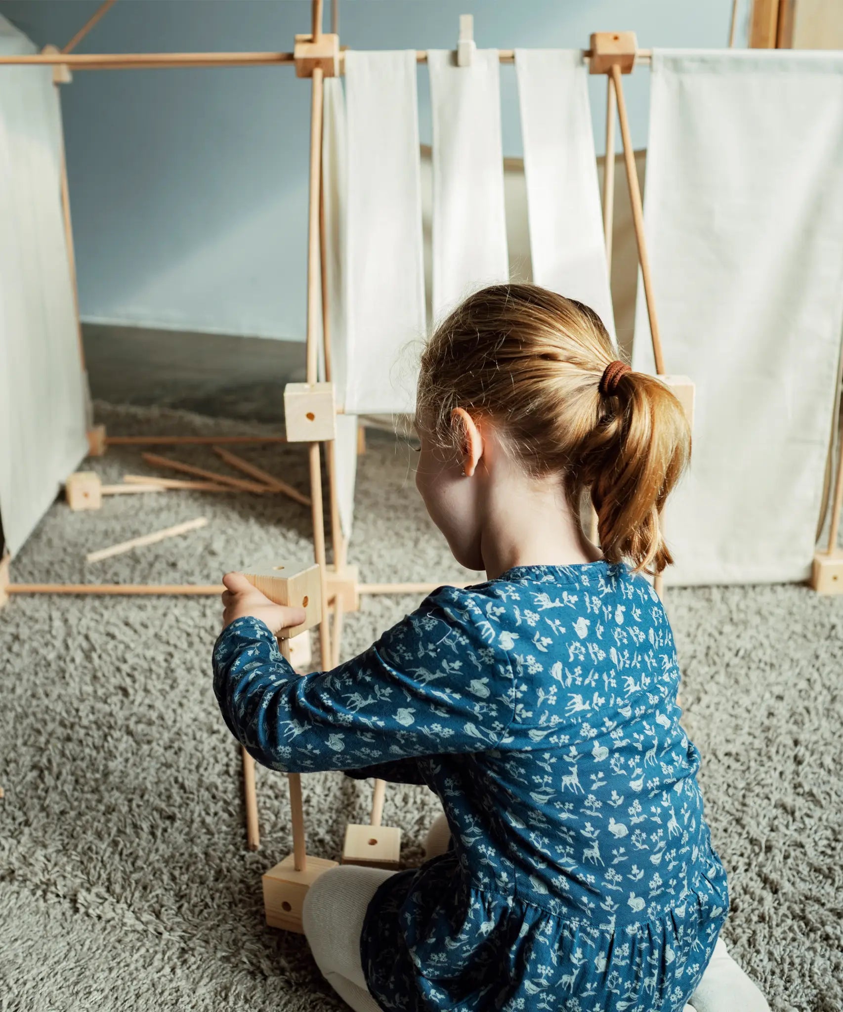 Child building using wooden poles and blocks from the Trigonos kernel organic family construction set