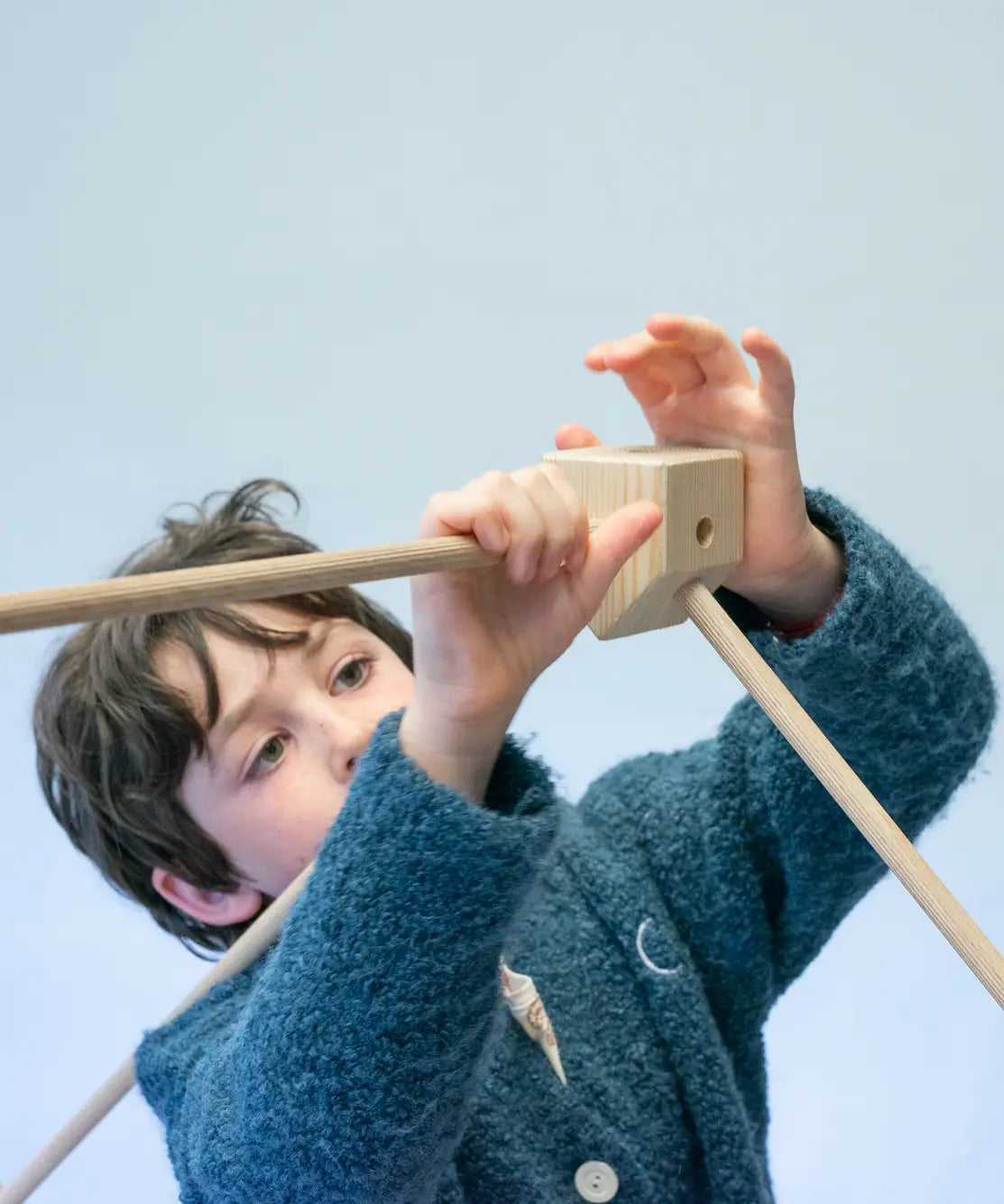 Child placing wooden poles into a corner block for the roof used from the Trigonos kernel organic set