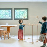 Children building a a tent structure using the Trigonos wooden kernel organic construction set in a dining room setting